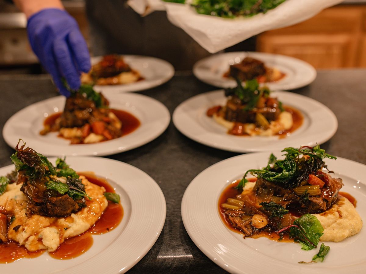 Chef finishing plates of braised meat over mashed potatoes in the Double P Ranch lodge kitchen